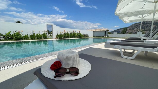 A poolside area with a white hat, sunglasses, and a red rose on a lounge chair. - VILLA ALTUN 1 (Mugla)