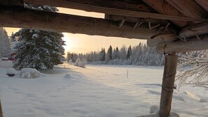 Paisatge nevat amb una construcció de fusta, possiblement una cabana, i un arbre cobert de neu.