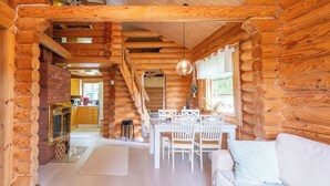 Interior d'una cabana de fusta amb zona de menjador, mobles blancs i una llar de foc.