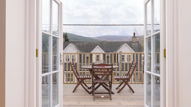 Un balcon ouvert avec une table et des chaises en bois, une vue sur des maisons au loin et une clôture en bois.