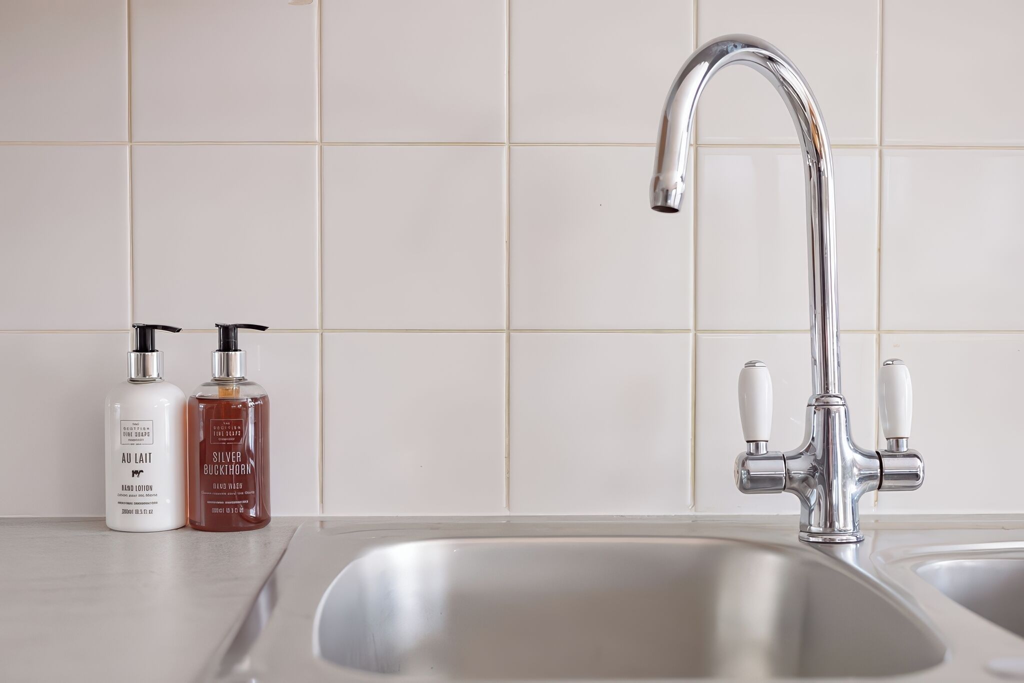 A modern kitchen with a stainless steel sink, two bottles of hand soap, and a chrome faucet.