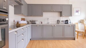 Une cuisine moderne avec des meubles gris, un four encastré et un coin repas en bois.