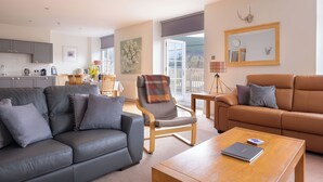 Un salon moderne avec un canapé gris, un divan en cuir marron et une table basse en bois. On aperçoit à l’arrière-plan un coin repas avec une table et des chaises.