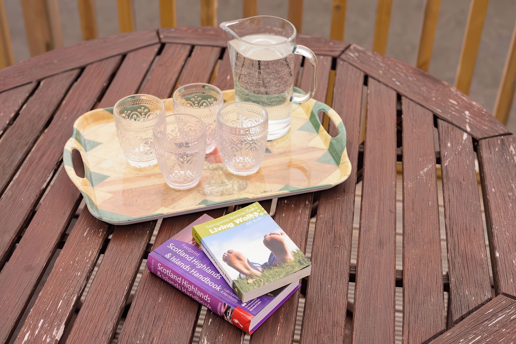 A wooden table with a tray holding a pitcher and four glasses, and two books titled 'Scotland & the Highlands Handbook' and 'Living Walls'.