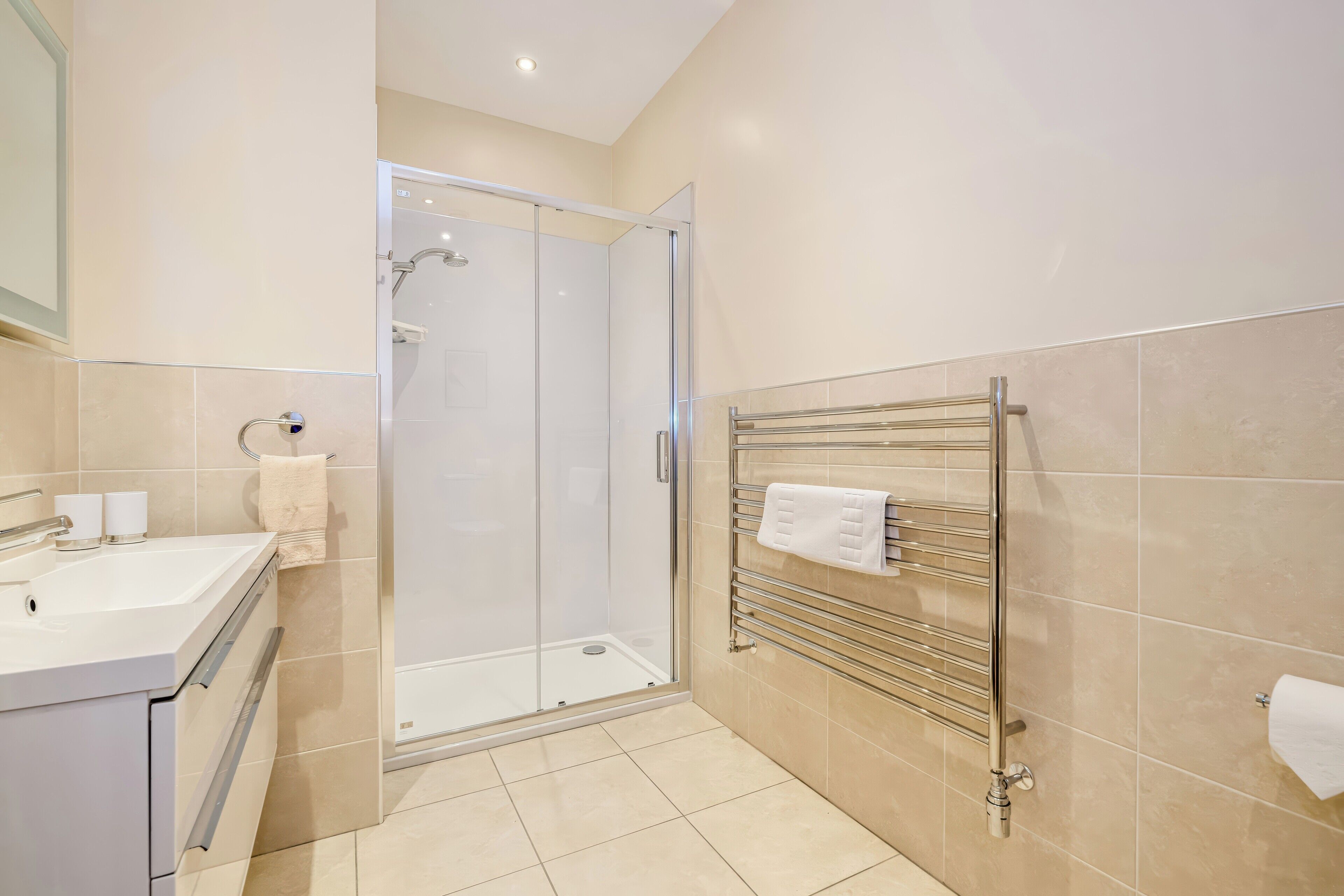 A modern bathroom with a glass-enclosed shower, a sink with a mirror, and a towel rack.