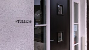 Une porte noire avec une enseigne portant l’inscription « TULLICH » et un mur blanc à la texture particulière.