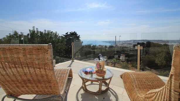 A balcony with wicker chairs, a glass table, and a view of a cityscape and water.