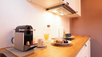 A kitchenette with a coffee machine, a glass of orange juice, a plate with pastries, and a coffee cup.