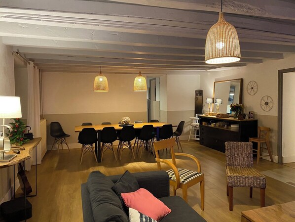 A cozy living room with a sofa, a dining table with chairs, a kitchen area, and a large mirror on the wall. - Large, charming house in L'ETALE, Meyran/La Hume (Gujan-Mestras)