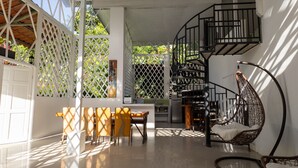A spacious indoor area with a dining table and chairs, a hanging chair, and a spiral staircase.