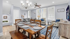 Un coin repas avec une table en bois dressée pour quatre personnes, un lustre et un ventilateur de plafond.