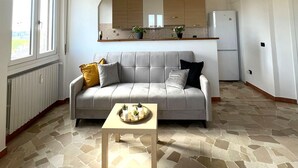 Una sala de estar con un sofá gris, una mesa de centro y una cocina al fondo.
