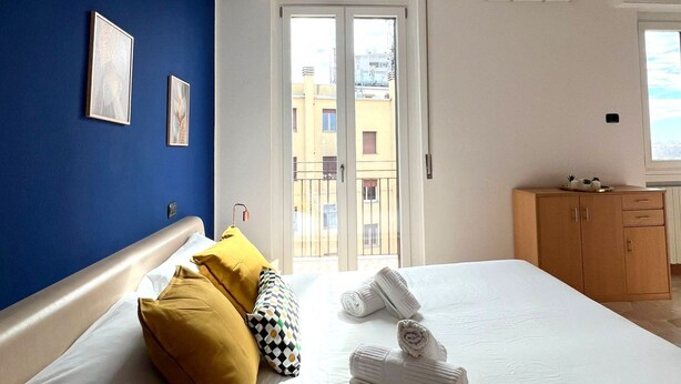 Un dormitorio con cama, armario y ventana con vistas a edificios.