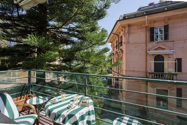 A balcony with wicker furniture, a table with a striped tablecloth, and a building with classical architecture in the background.