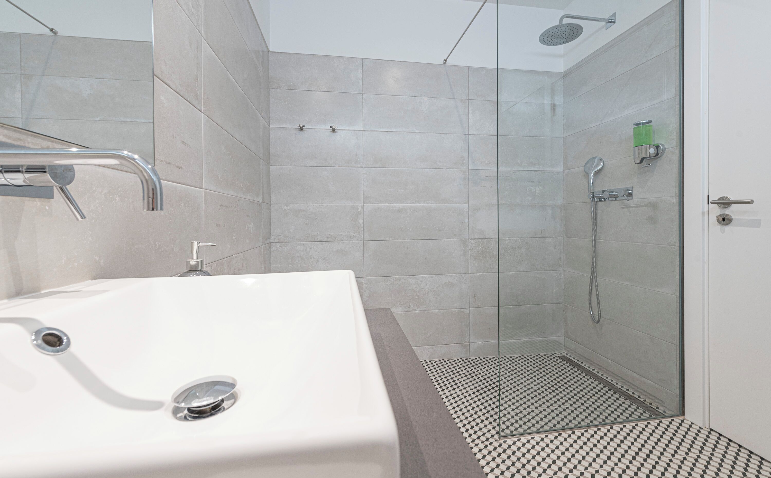 Um banheiro moderno com pia branca, chuveiro com porta de vidro e piso revestido de azulejos.