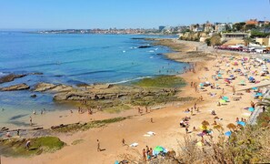 Une plage avec une eau d’un bleu limpide, des zones rocheuses et des gens qui prennent des bains de soleil.