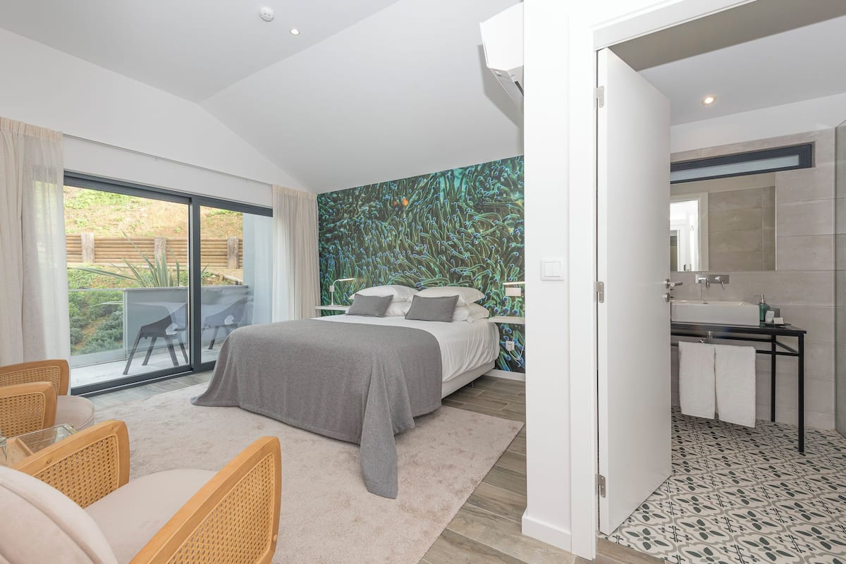 Un dormitorio con cama, un baño con lavabo y vistas a un jardín a través de una puerta corredera.