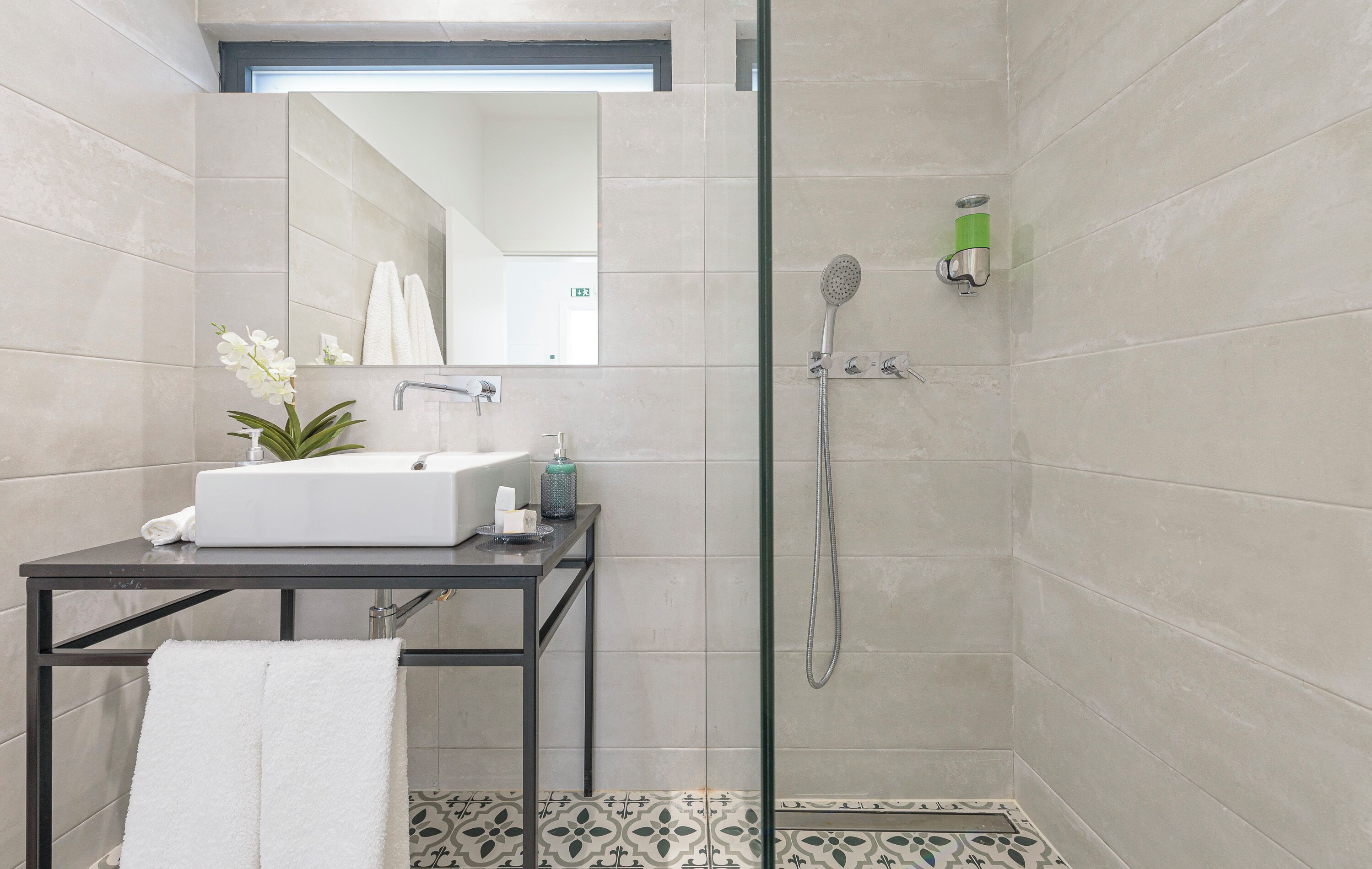 Un baño moderno con ducha de vidrio, un lavamanos con espejo y una mesita con una toalla.