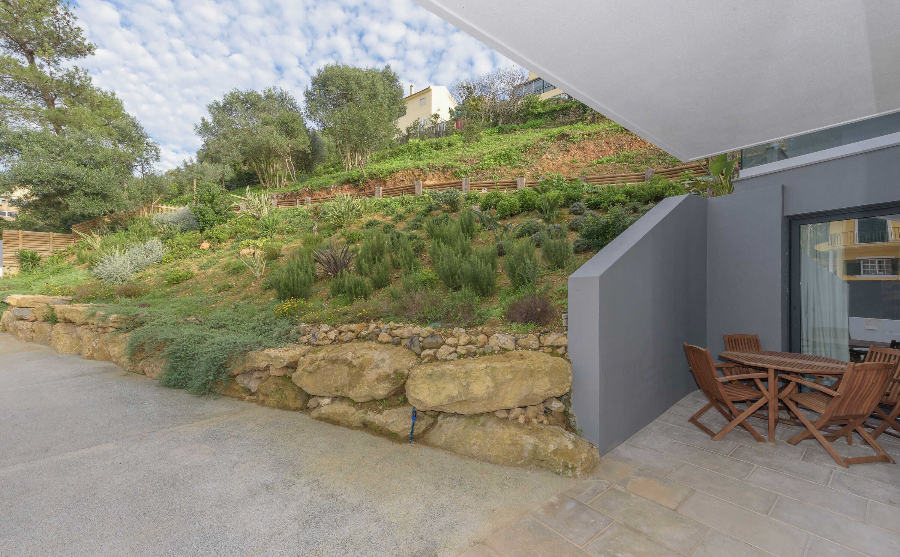 A modern outdoor patio with stone walls, a wooden fence, and a variety of plants.