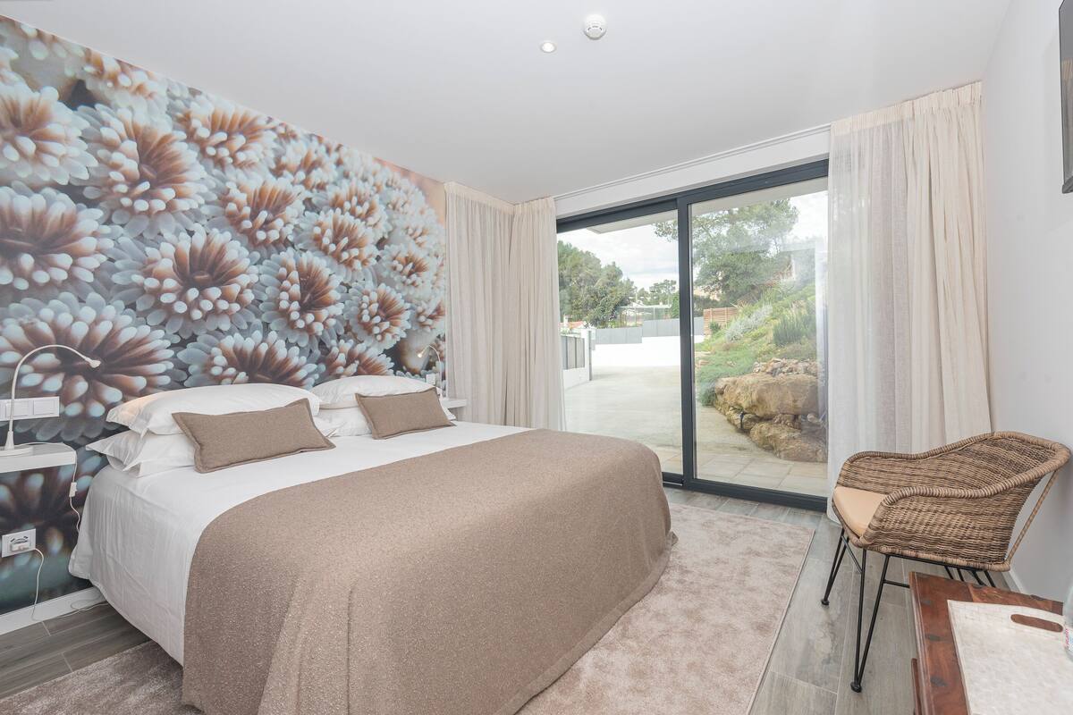 Un dormitorio con una cama grande, una silla, una mesita de noche y un mural de flores en la pared.