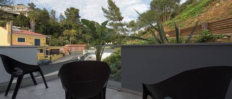 Un balcone con due sedie nere, vista su una zona residenziale con case e alberi, e un cielo sereno.