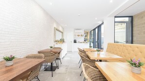 Una cocina moderna con armarios blancos, un comedor con mobiliario de mimbre y un amplio ventanal que proporciona luz natural.