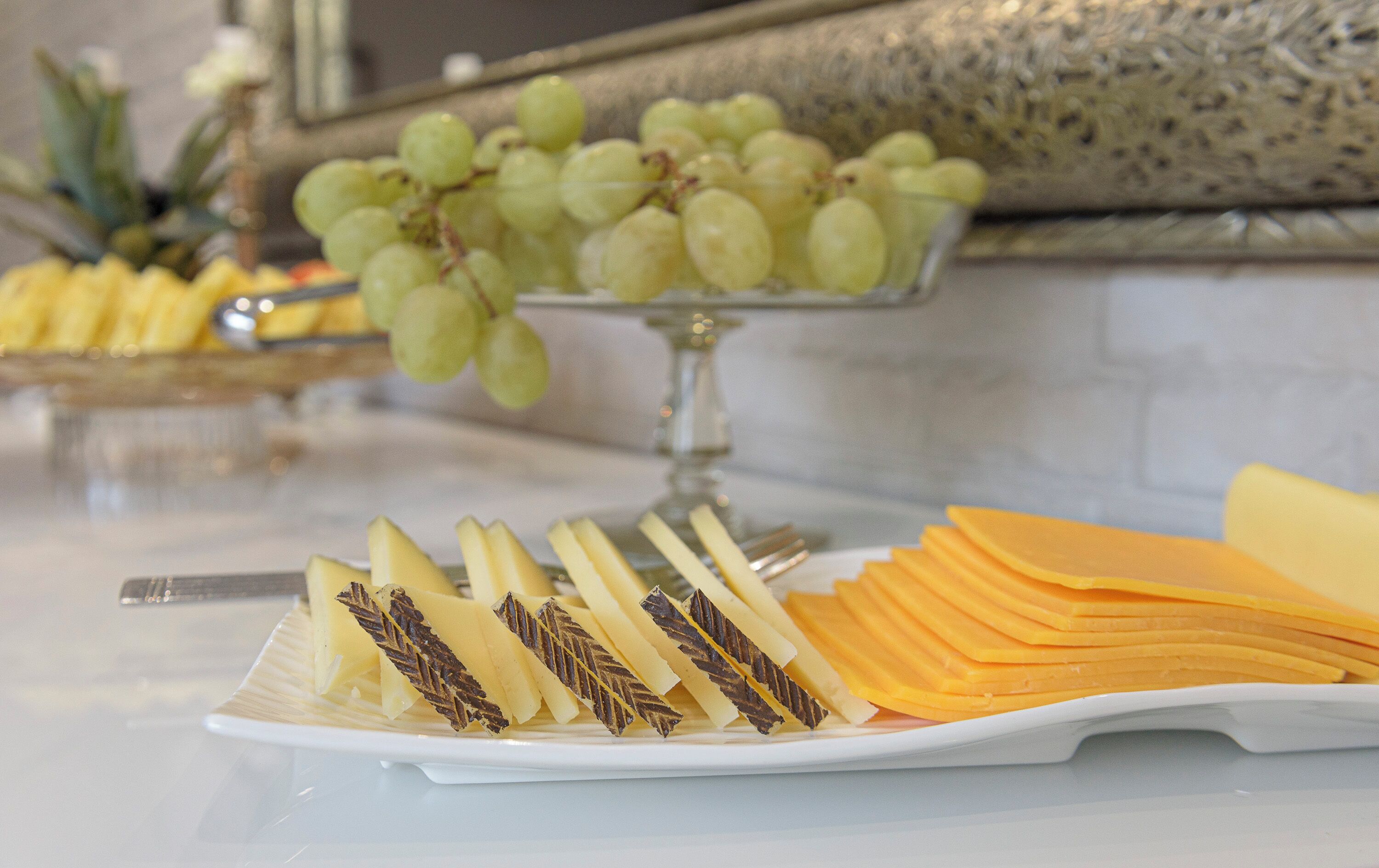 A buffet with sliced cheese, grapes, and a decorative leaf pattern on the cheese.