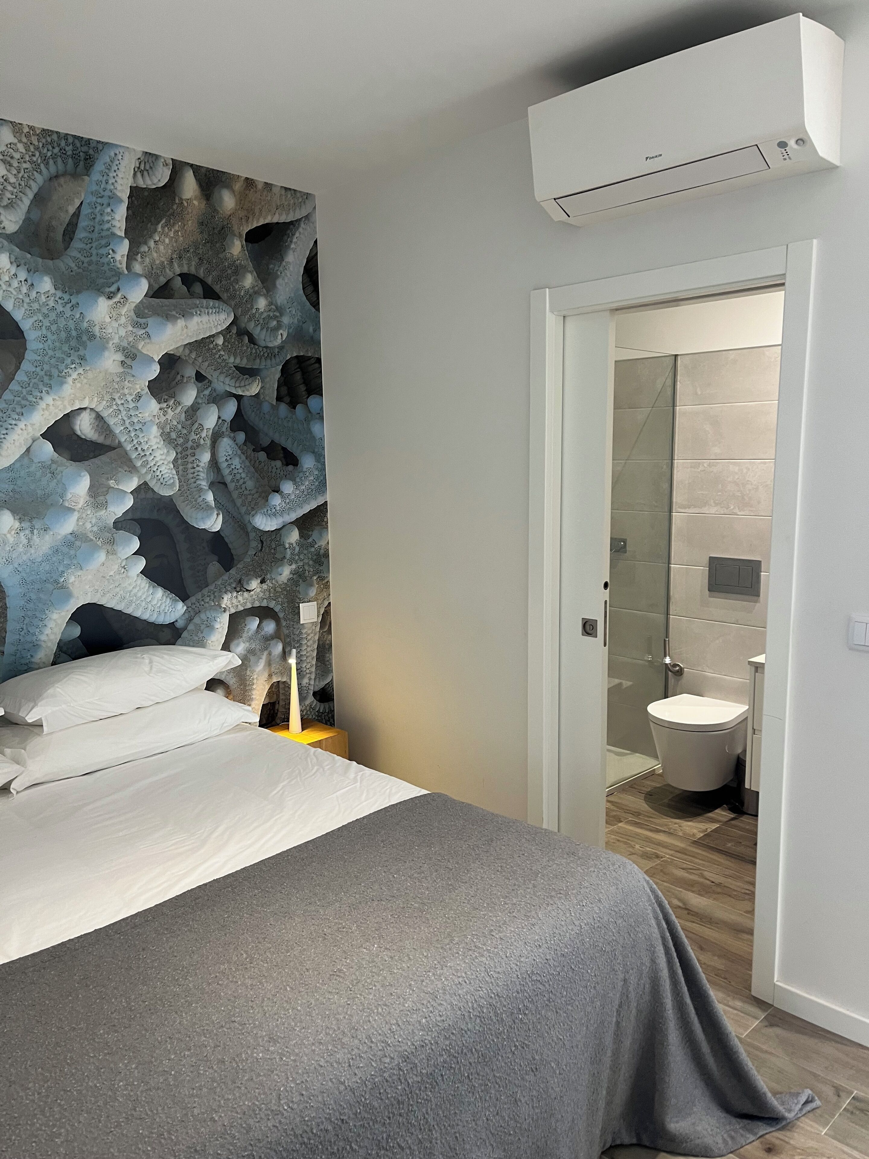 A modern bedroom with a large bed, a textured wall, and a bathroom visible through an open door.