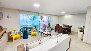 A living room with a sofa, chairs, a dining table, and a view of the ocean.