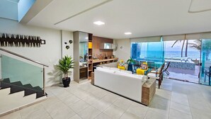 A modern hotel lobby with a reception desk, seating area, staircase, and a view of the ocean.