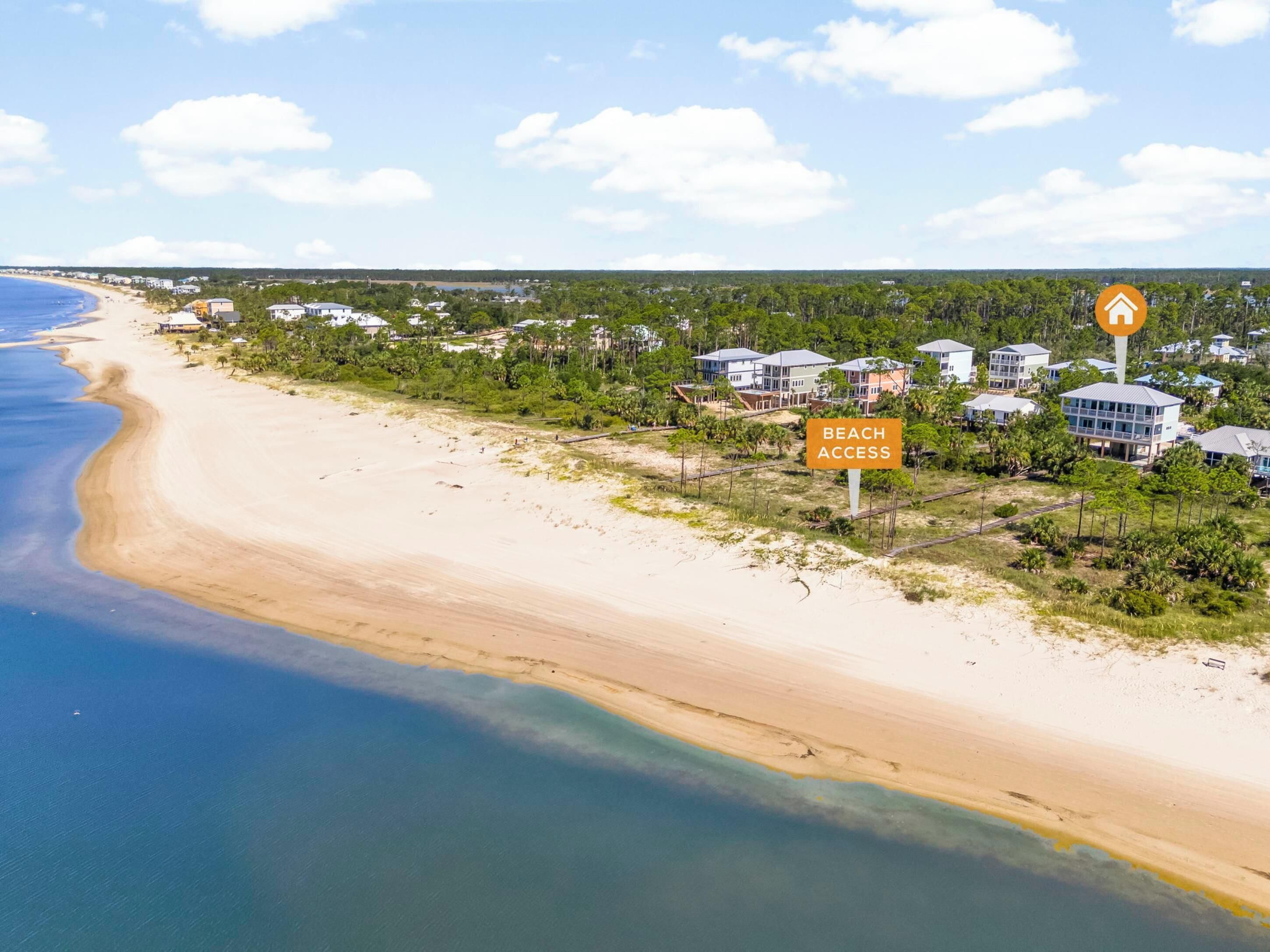 Un quartier résidentiel situé sur la côte, avec des propriétés donnant sur la plage, un ciel dégagé et un panneau indiquant l’accès à la plage.