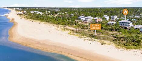 Un quartier résidentiel situé sur la côte, avec des propriétés donnant sur la plage, un ciel dégagé et un panneau indiquant l’accès à la plage.