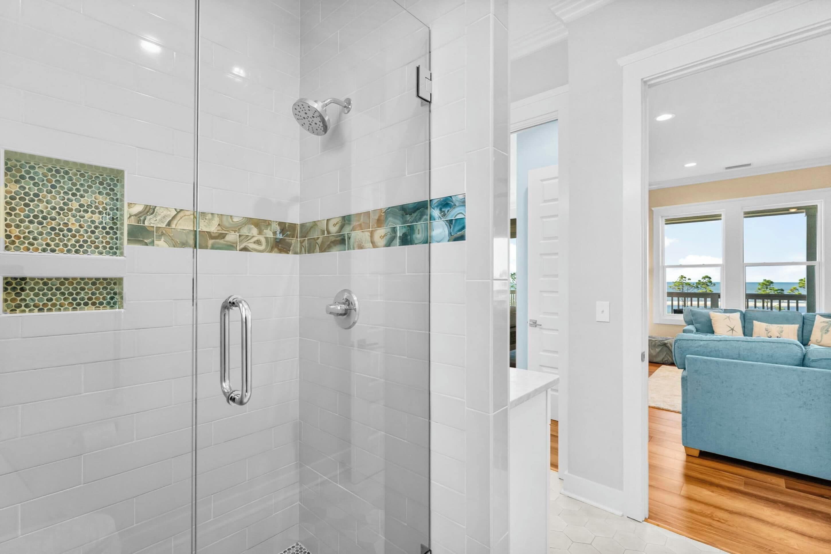 A modern bathroom with a glass-enclosed shower, white tiled walls, and a blue patterned tile accent.