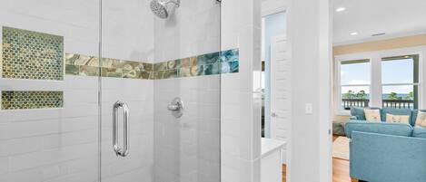 A modern bathroom with a glass-enclosed shower, white tiled walls, and a blue patterned tile accent.