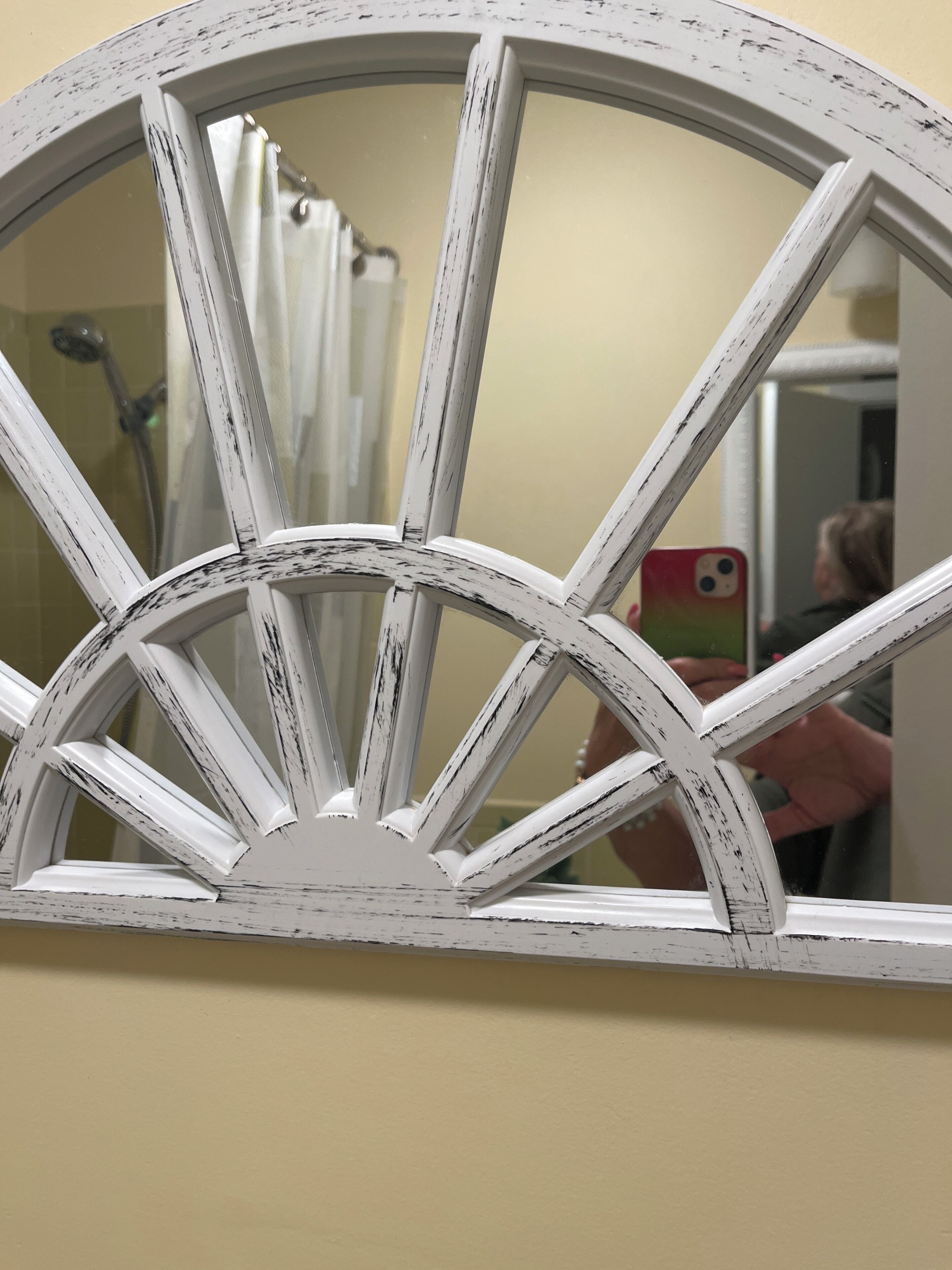 Een witte, verweerde houten constructie die op een wiel lijkt, waarschijnlijk een decoratief element of onderdeel van een deurkozijn.