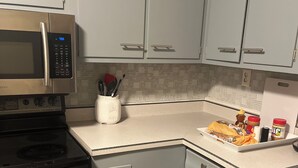 Una cocina con armarios grises, un microondas de acero inoxidable, una estufa negra y una encimera blanca con un tostador y utensilios de cocina.