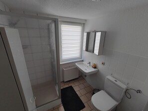 Un baño con ducha, inodoro, lavamanos y ventana.