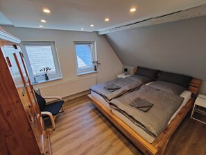 Un dormitorio con cama elevable, dos ventanas, un radiador, un escritorio y una silla.
