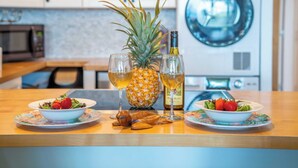 Keittiön työtasolla on kaksi kulhoa täynnä mansikoita ja yksi ananas, pullo viiniä sekä lasi viiniä.