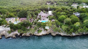 Vista aérea de una propiedad costera con varias casas, una piscina y abundante vegetación.