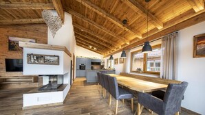 Une cuisine spacieuse avec un plancher en bois, un coin repas avec une longue table et des chaises, et une grande fenêtre avec des rideaux.