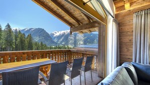 Une terrasse en bois avec une table et des chaises, offrant une vue sur un paysage montagneux.