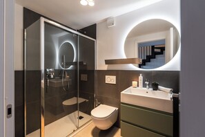 A modern bathroom with a glass-enclosed shower, a toilet, and a sink with a mirror above.