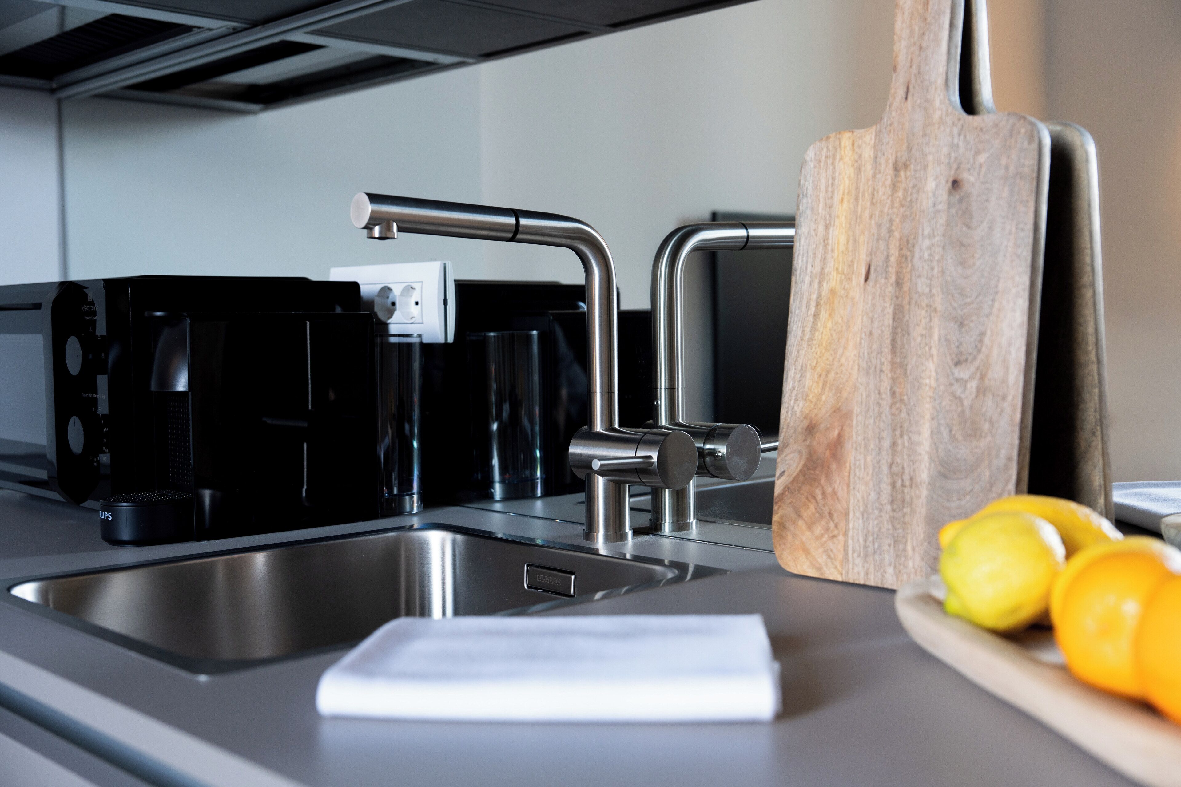 Une cuisine moderne équipée d’appareils électroménagers en acier inoxydable, d’une planche à découper en bois et d’un saladier rempli de citrons.
