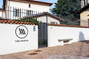 A villa with a white exterior, a black gate, and a cobblestone driveway.