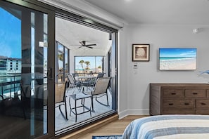 Ein Schlafzimmer mit einer großen Schiebetür zu einem Balkon mit Pool, Deckenventilator, Bett, Kommode und zwei gerahmten Bildern.