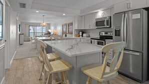A modern kitchen with a central island, stainless steel appliances, and wooden chairs.