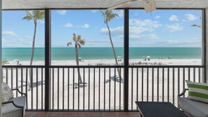 A balcony with a view of a beach, palm trees, and a clear sky.