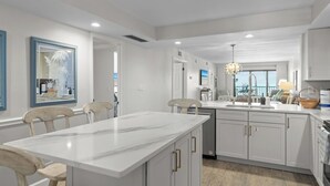 A modern kitchen with white cabinetry, a marble island, and a view to the outside.