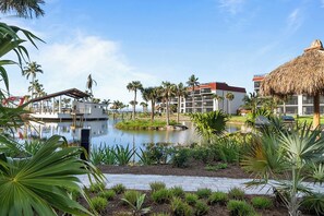 A resort with a central water feature, palm trees, and modern buildings with a thatched roof structure.